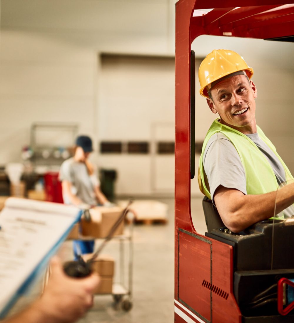 Happy forklift driver communicating with dispatcher in industrial warehouse.